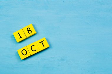 Mavi ahşap yüzeyde, 18 Ekim tarihli sarı küpler takvimi ve kopyalama alanı
