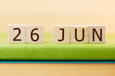 Wooden cubes calendar for 26 JUNE on green book, closeup