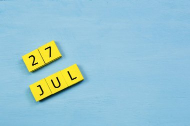 Mavi ahşap yüzeyde, 27 Temmuz 'lu sarı küpler takvimi ve kopyalama alanı