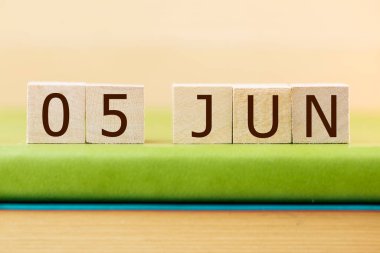 Wooden cubes calendar for 05 JUNE on green book, closeup