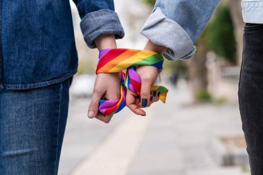 İki kişi el ele tutuşmuş, gökkuşağı desenli eşarplar takıyor. Eşarp, LGBTQ toplumuna sevgi ve kabulü temsil eden gökkuşağı gurur hareketinin bir sembolüdür..