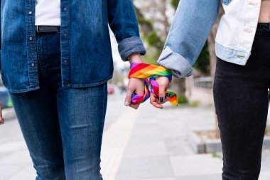 İki kişi el ele tutuşmuş, gökkuşağı desenli eşarplar takıyor. Eşarp, LGBTQ toplumuna sevgi ve kabulü temsil eden gökkuşağı gurur hareketinin bir sembolüdür..