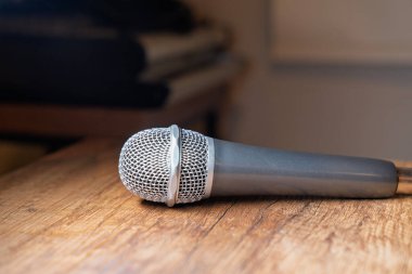Dinamik mikrofon, rahat bir ortamda ahşap bir masada yatıyor. Müzik kaydı, podcast veya canlı performans hazırlama kavramı.