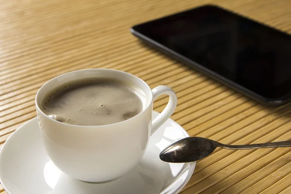 Tasse à café et tablette sont sur une table lumineuse en bambou . — Photo