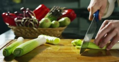 hands of a young cook cut a fresh onion and leeks in slowmotion