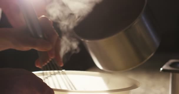 Super slow motion macro of a middle aged chef pouring hot milk from a pot in a bowl (close up) — 비디오