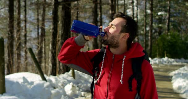 Beau jeune homme s'arrête pour regarder la nature autour et respirer continuellement vers le bas pour se tourner sur lui-même dans un fond naturel et porter un sweat-shirt rouge et boire de l'eau douce — Video