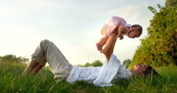 Super lent mouvement de la jeune mère caucasienne couchée sur l'herbe et jouer avec son bébé fille dans une prairie de vignoble sur un soleil dans 4k — Video