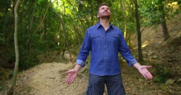 Schöner junger Mann hält an, um die Natur ringsum zu betrachten und atmet kontinuierlich nach unten, um sich vor einem natürlichen Hintergrund einzuschalten — Stockvideo