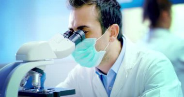young and charming doctor look in microscope accomplishes some routine medical procedures and equipped professional in the laboratory researcher with professional development materials