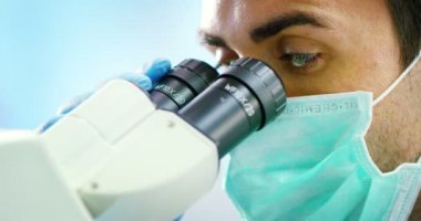 young and charming doctor look in microscope accomplishes some routine medical procedures and equipped professional in the laboratory researcher with professional development materials