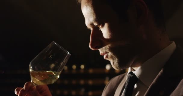 Mouvement lent du jeune sommelier vêtu d'une veste formelle et des odeurs de cravate et essaie le vin blanc versé dans un verre transparent dans une cave à vin sombre 4k (gros plan ) — Video