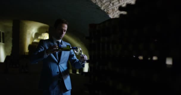 慢动作的年轻侍酒师穿着正式的夹克和领带的气味和试图白葡萄酒倒在透明的玻璃，在黑暗的酒窖 4 k — 图库视频影像