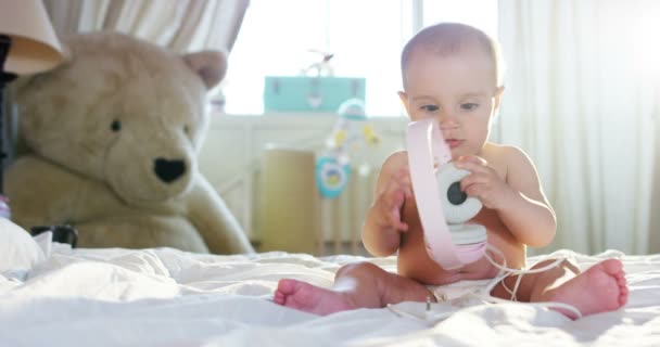En söt liten baby tittar in i kameran och är klädd i en rosa hörlurar barnet ser sig omkring och sedan ler och skrattar. — Stockvideo