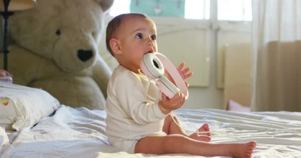 Ein süßes kleines Baby schaut in die Kamera und trägt einen rosa Kopfhörer, das Baby schaut sich um und lächelt und lacht. — Stockvideo