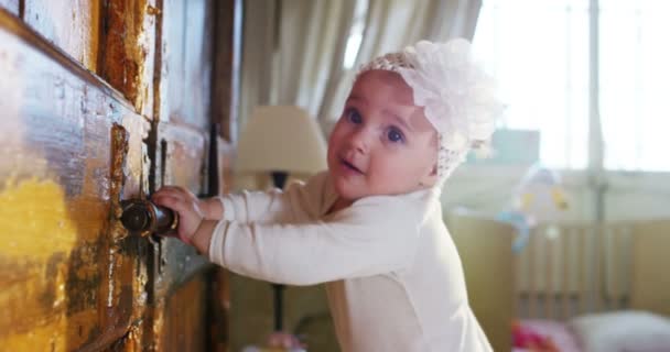Un bebé pequeño y lindo está mirando a la cámara y lleva una raya blanca con una flor, el bebé mira a su alrededor y juega con expresiones faciales — Vídeo de stock