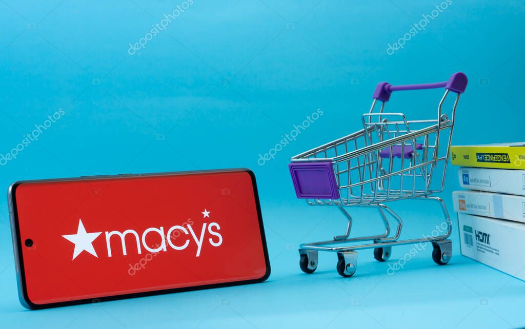 Dhaka, Bangladesh- 03 July 2025: Smartphone with Macy's logo next to a small shopping cart and boxes against a blue background.