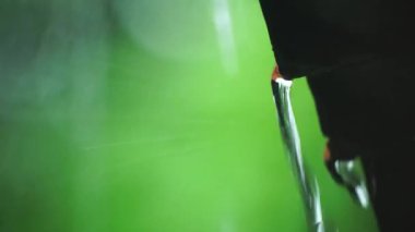 Teneke çatının kenarından şiddetli yağmur yağıyor. Arka plandaki yeşil yapraklar bulanık..