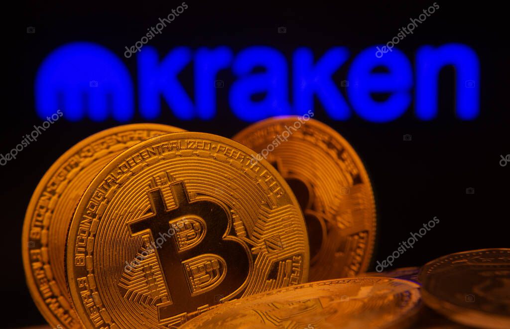 Dhaka, Bangladesh- 01 Nov 2025: Close-up of Bitcoin coins with the Kraken logo visible on a screen in the background.