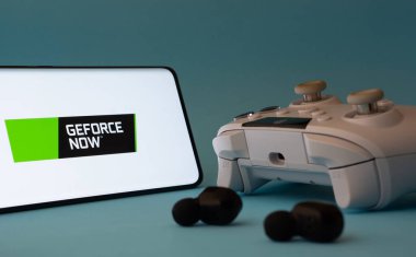 Dhaka, Bangladeş - 23 Mar 2025: Bir Geforce Now simgesine sahip bir akıllı telefon mavi bir yüzey üzerinde bir denetleyici ve kulaklıklar.