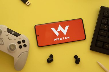 Dhaka, Bangladeş - 22 Mar 2025 Webzen logolu akıllı telefon, oyun denetleyici ve arka planda kulaklık.