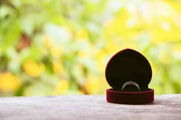 Red gift box with ring on background of greenery and flowers. Selective focus, toned image, film effect, macro, close-up — Stock Photo, Image