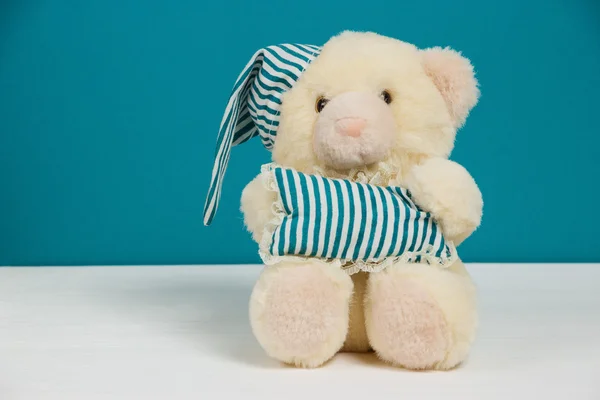 Joli ours beige avec un bonnet de nuit et un oreiller sur fond blanc et bleu. Mise au point sélective, image tonique, effet film, espace de copie, vue de niveau — Photo