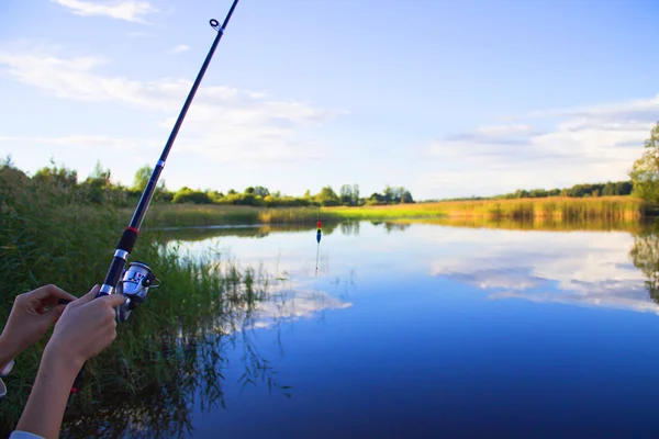 Caña de pescar en la mano sobre un fondo de lago — Foto de Stock
