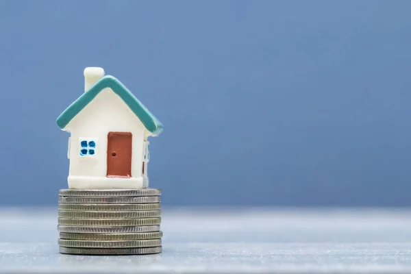 Small toy house on a stack of coins on a gray background. Housing, mortgage, loan concept.