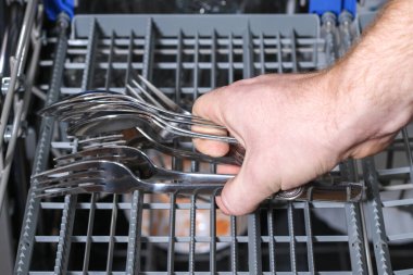 Bir adam bulaşık makinesine kirli bulaşıkları, tabakları, kaşıkları, çatalları, çatal bıçakları koyuyor..