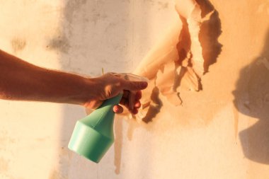 Bir adam eski duvar kağıdını bir spatula ve su dolu bir spatulayla temizler..