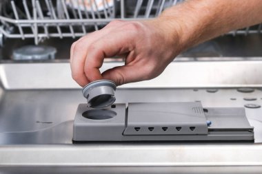 Bir adam bulaşık makinesinin kompartımanına durulama malzemesi döker..