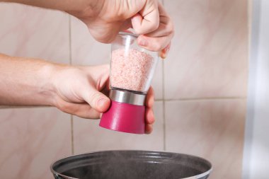 Bir adam Himalaya tuzuyla çorbayı tuzlar el değirmeninden.