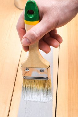 Elinde boya olan fırça. Bir adam tahta tahtaları gri boya fırçasıyla boyuyor..