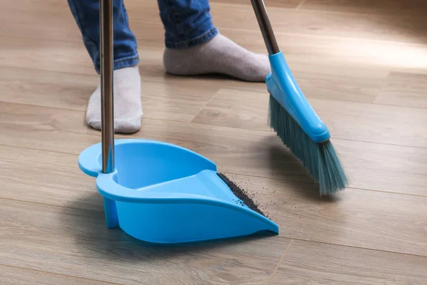 The man sweeps the debris into a blue scoop with brush. — Stock Photo, Image