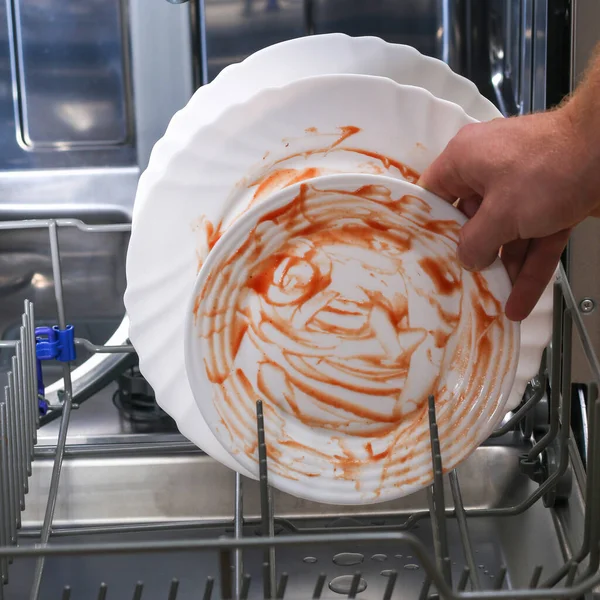 Um homem carrega pratos sujos, pratos, colheres, garfos, talheres na bandeja da máquina de lavar louça. — Fotografia de Stock