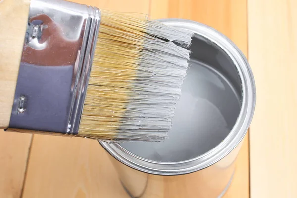 Brush with can paint in hand. A man paints wooden boards in gray paint brush.
