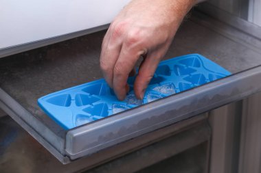 A man takes ice from a freezer tray freeze low food in one layer. clipart