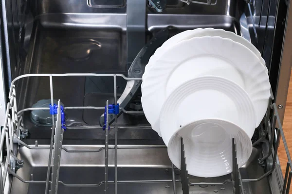 Мужчина загружает грязную посуду, тарелки, ложки, вилки, столовые приборы в посудомоечную машину. — стоковое фото