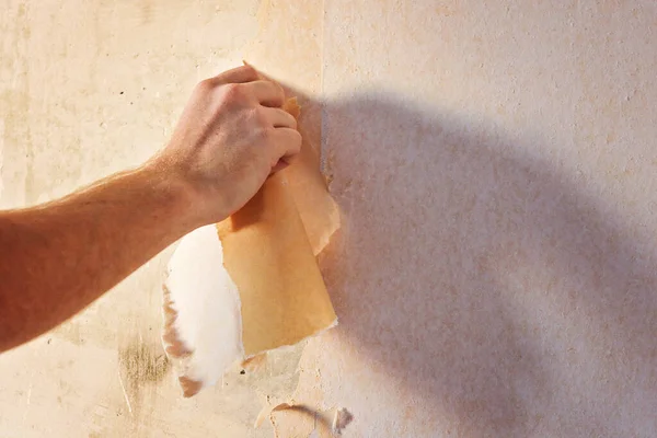 Um homem remove papel de parede velho com uma espátula e spray garrafa com água. — Fotografia de Stock