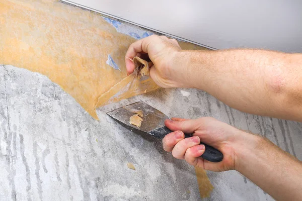 A man removes old wallpaper with a spatula and spray bottle with water.