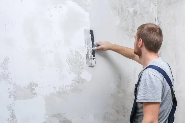 Ein männlicher Arbeiter verteilt die Spachtelmasse und glättet die Wand. — Stockfoto