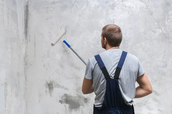 Um trabalhador masculino primes parede com rolo para melhor aderência. — Fotografia de Stock