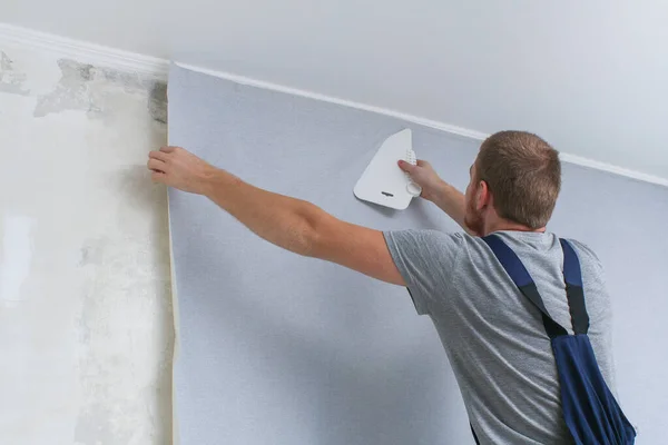 Homem cola papel de parede de vinil cinza em um suporte não-tecido. Renovação da sala. — Fotografia de Stock