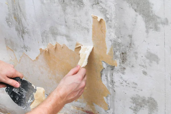 Um homem remove papel de parede velho com uma espátula e spray garrafa com água. — Fotografia de Stock