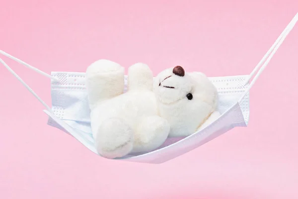The white teddy bear is swinging in a medical mask like in hammock or swing. — Stock Photo, Image