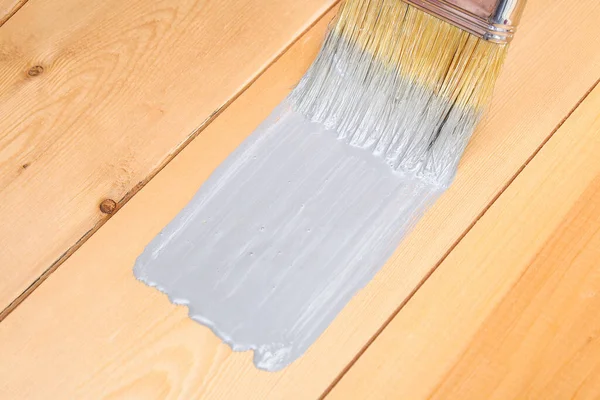 Escova com pode pintar na mão. Um homem pinta tábuas de madeira em pincel de tinta cinza. — Fotografia de Stock