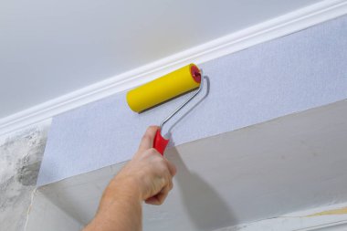 Adam, gri vinil duvar kağıdını dokunmamış bir desteğe yapıştırıyor. Odanın yenilenmesi.