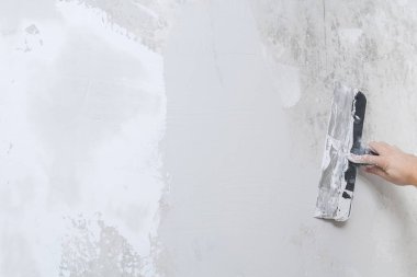 Erkek bir işçi macun karışımını yayar ve duvarı düzleştirir..