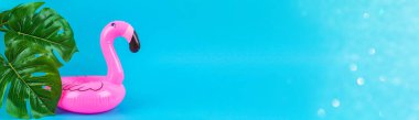 Mavi arka planda şişme pembe flamingo ve canavar yaprakları var..